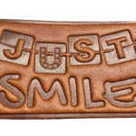 Custom engraved leather patch featuring the 'Just Smile' design with embossed lettering, premium brown faux leather, stitched border, and rectangular finish for hats, jackets, and bags