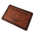Custom embossed leather patch featuring the LIKE JS Fashion Jeans logo with premium brown faux leather, engraved branding, decorative border, and rectangular design for jackets, jeans, hats, and bags